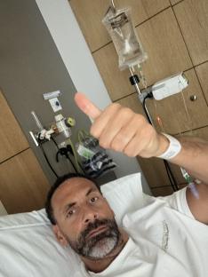 Man in hospital bed giving thumbs up.