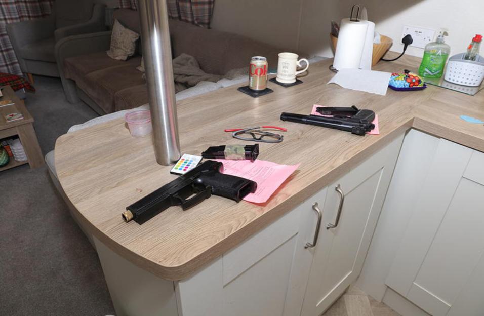 Crime scene photo of two imitation handguns, an ammunition magazine, and other items on a kitchen counter in a caravan.