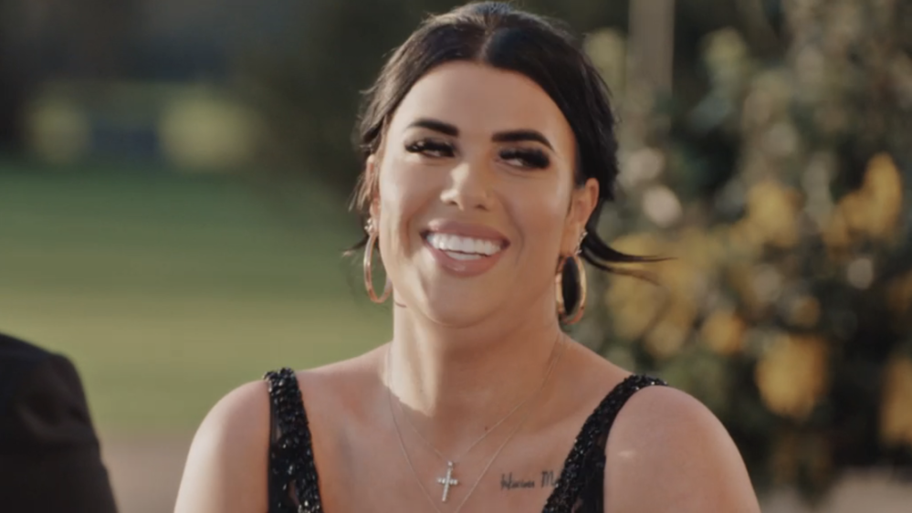 A smiling woman with dark hair and a cross necklace.