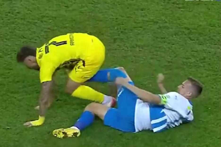 Nicusor Bancu in a yellow jersey falling near a player in a blue and white jersey on a green grass field.