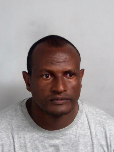 A man with dark skin and a receding hairline looking directly ahead in a mugshot.