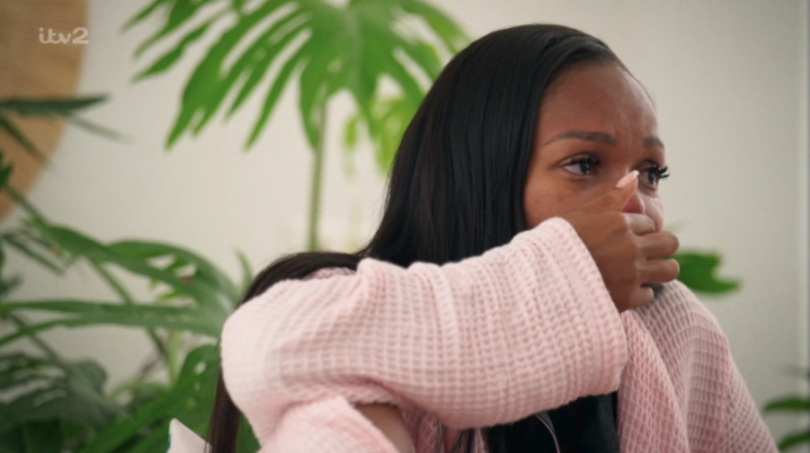 A woman in a pink robe crying, covering her mouth with her hand.