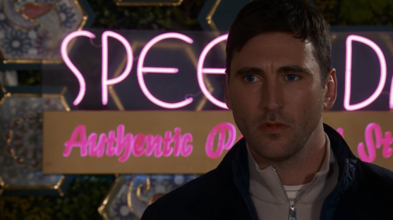 Man standing in front of a pink neon sign that says