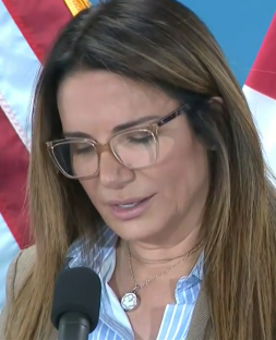 A woman wearing glasses speaks into a microphone.