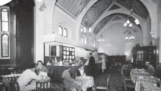 Black and white photo of a pub in a railway station waiting room.