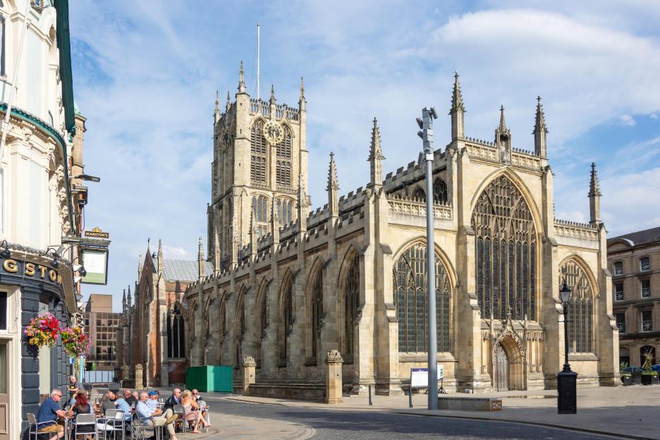 Hull Minster, a large Gothic church with a prominent clock tower, and a group of people seated at outdoor tables of a nearby pub.