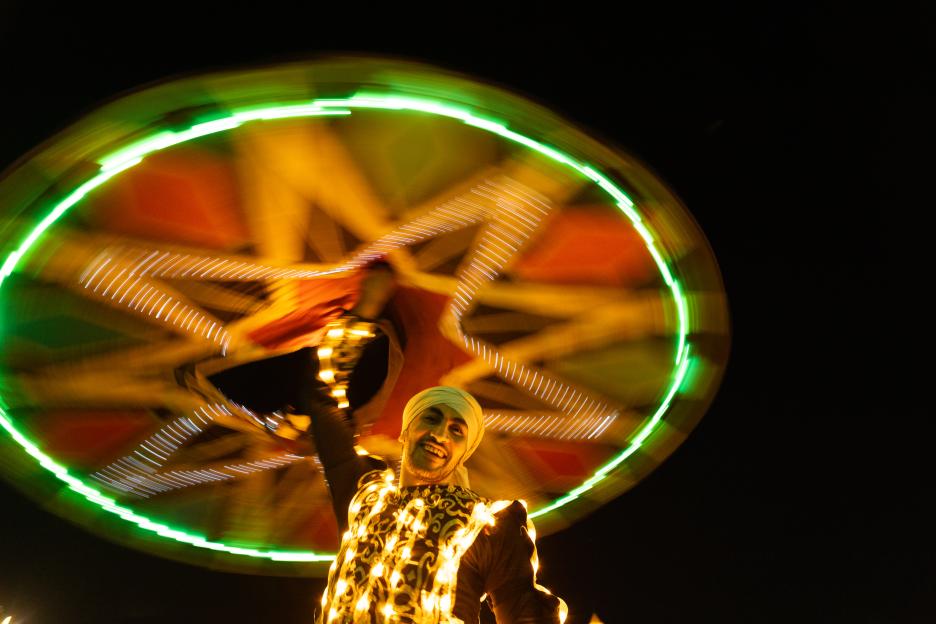 A tan-skinned man in a turban smiles while spinning a glowing wheel of light.