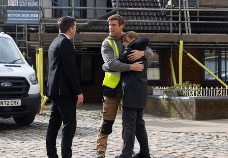 Scene from Coronation Street showing Todd Grimshaw embracing a woman while a man in a suit looks on.