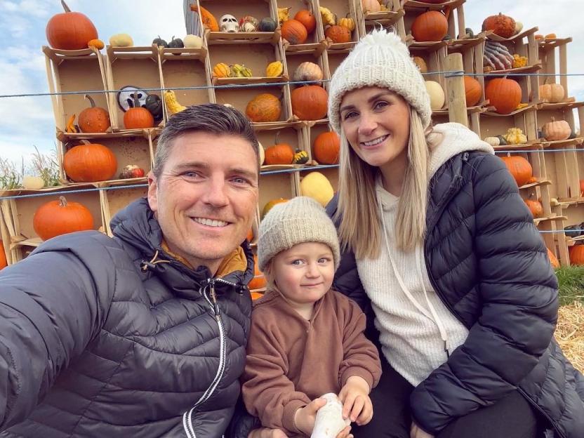 Asa Elliott with his wife and child in front of a pumpkin display.