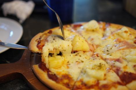 Hawaiian pizza with ham, bacon, and pineapple being served with a spoon.