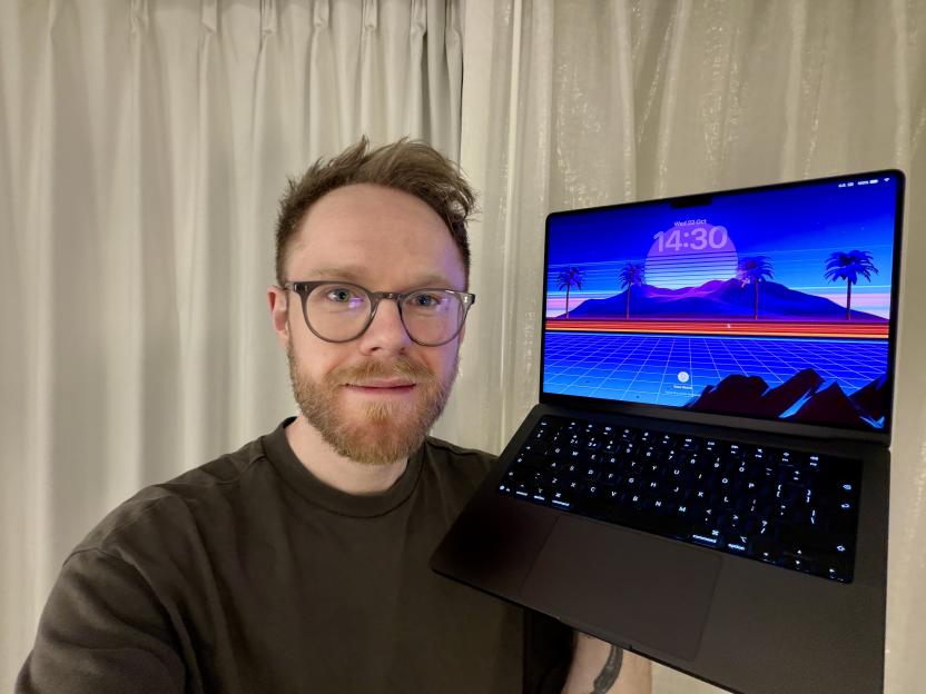 Man in glasses holding a laptop displaying a retro landscape with palm trees.