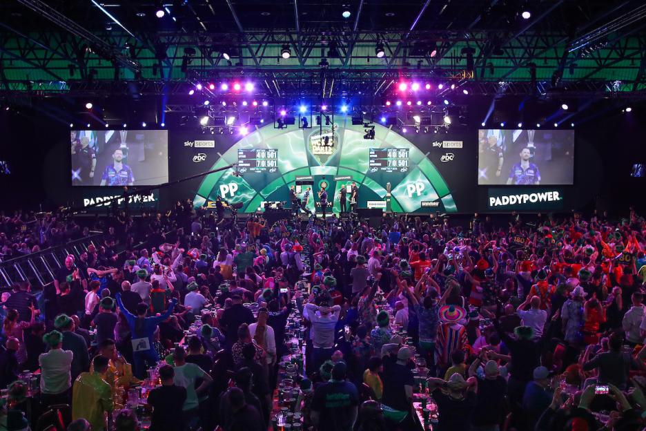 A large crowd cheering at a darts tournament.