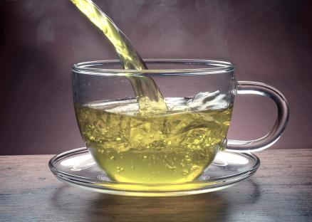 Green tea pouring into a glass cup.