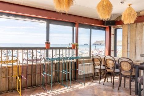 Beach view from a restaurant with colorful stools and wooden chairs.