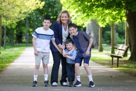 A woman and her three sons smiling for a photo in a park.