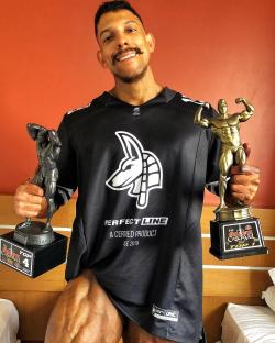 Bodybuilder Guilherme Henrique holding three bodybuilding trophies.