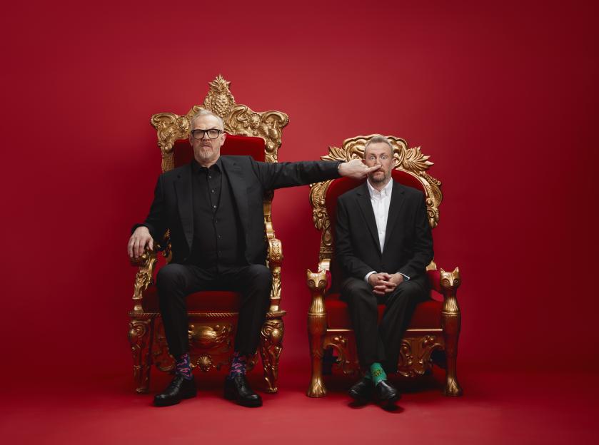 Greg Davies and Alex Horne seated in ornate gold chairs against a red background.