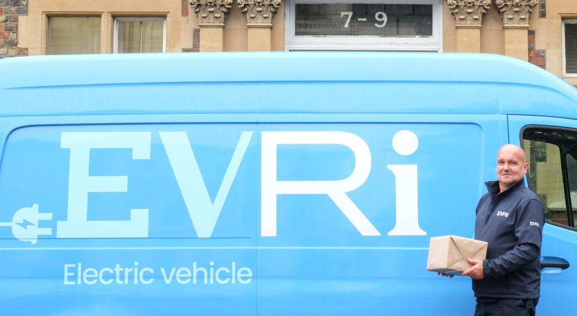 An Evri employee holds a parcel in front of a blue Evri electric delivery van.