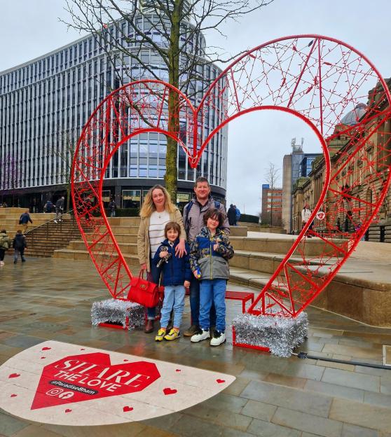 Family posing in front of a heart-shaped light display.