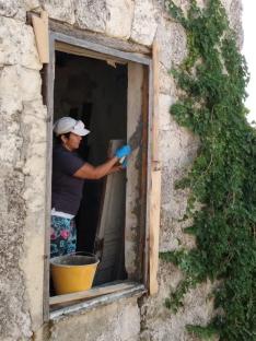 Woman repairing a window frame in a stone building.