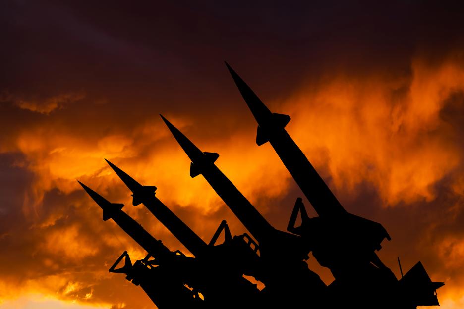 Three ballistic missiles in silhouette against a dramatic sunset sky.