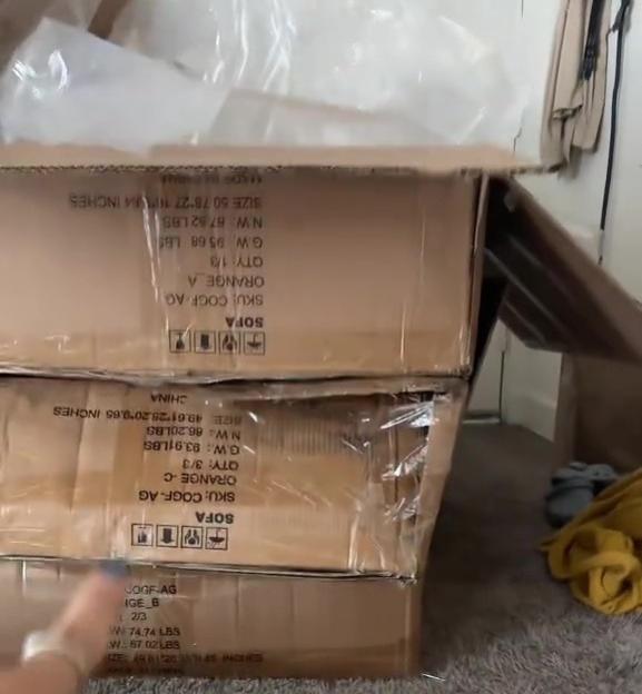 Cardboard boxes containing parts for a sofa, with text overlay "BUILDING THAT COUCH YOURSELF".