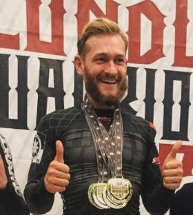 Man smiling and giving thumbs up, wearing medals.