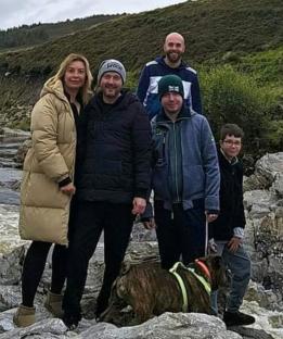 Family photo of a father, mother, three sons, and a dog near a river.