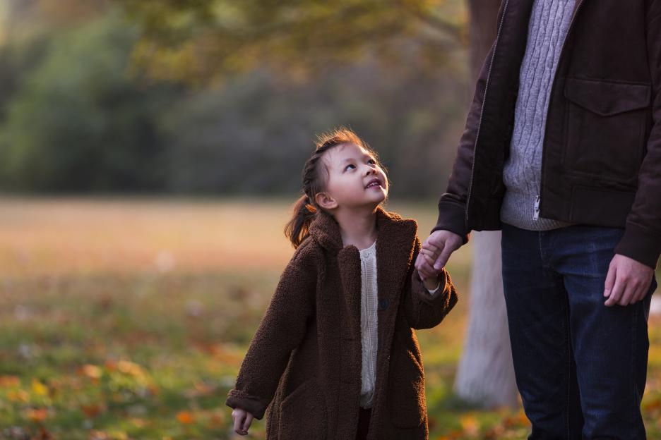 A young girl in a brown coat holding an adult's hand and looking up.