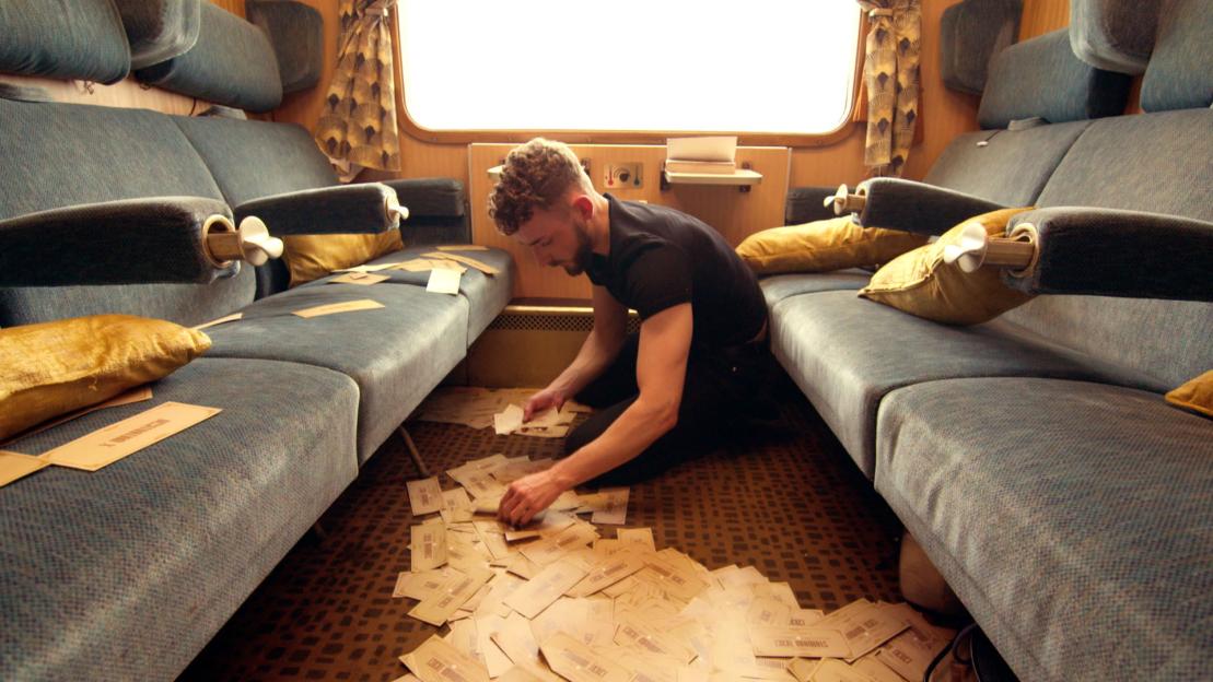 Man gathering scattered train tickets on a train floor.