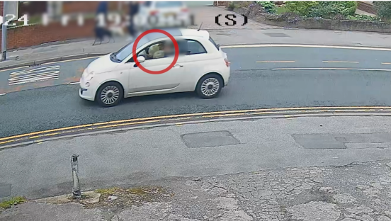 Screenshot of a white Fiat 500 driving down a residential street.