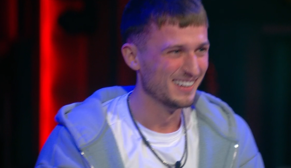 A man with short brown hair, wearing a grey hoodie and white shirt, smiling.