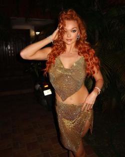 Woman with long red hair wearing a gold sparkly two-piece outfit.