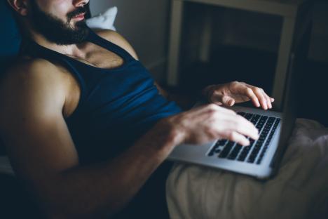 Young man using a laptop in bed at night.