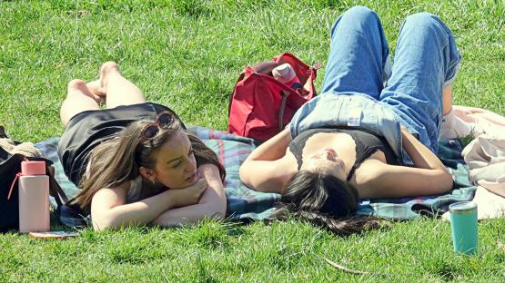 Two women relaxing on a blanket in a park.