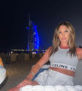 Woman in a Celine top and white shorts sitting outside at night with the Burj Al Arab in the background.