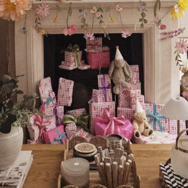 A fireplace mantel adorned with "HAPPY BIRTHDAY" balloons, surrounded by numerous wrapped presents.