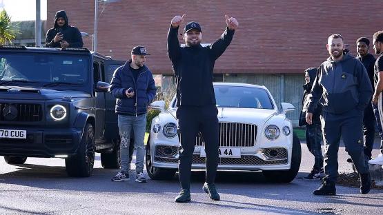 A man giving a thumbs up, standing between a black Mercedes G-Wagon and a white Bentley.