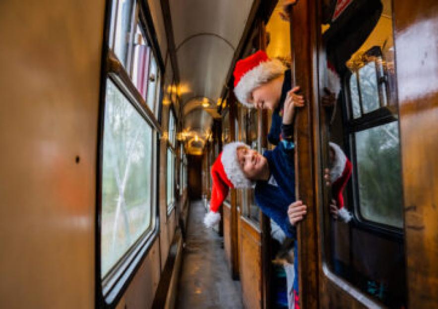 Two children wearing Santa hats lean out of a train window.