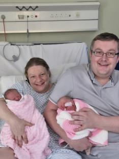 Parents holding their newborn twin daughters in a hospital bed.