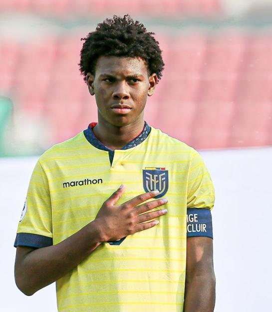 Soccer player in yellow jersey with hand over heart.