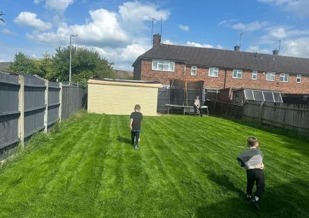 Photo of a backyard with newly seeded grass, a summer house, and children playing.
