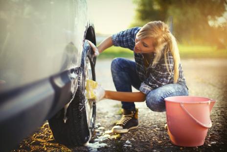 Woman washing car tire with sponge.