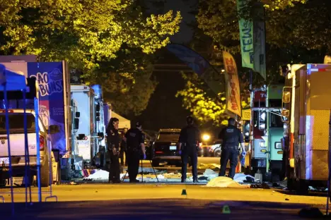 Crime scene with police officers and covered bodies near food trucks at night.