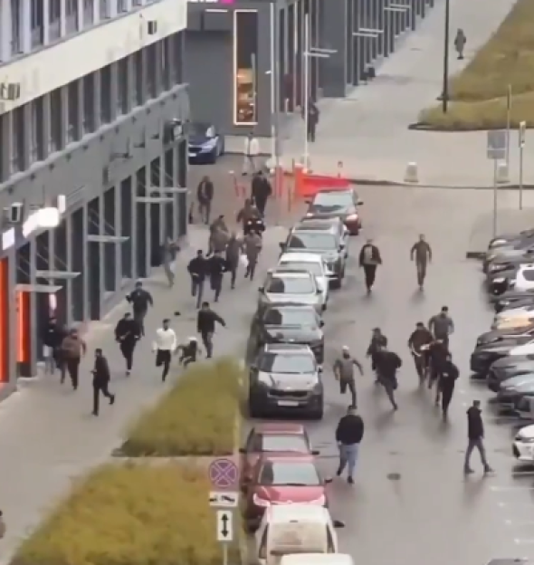 People running away from a building, with cars parked along the street.