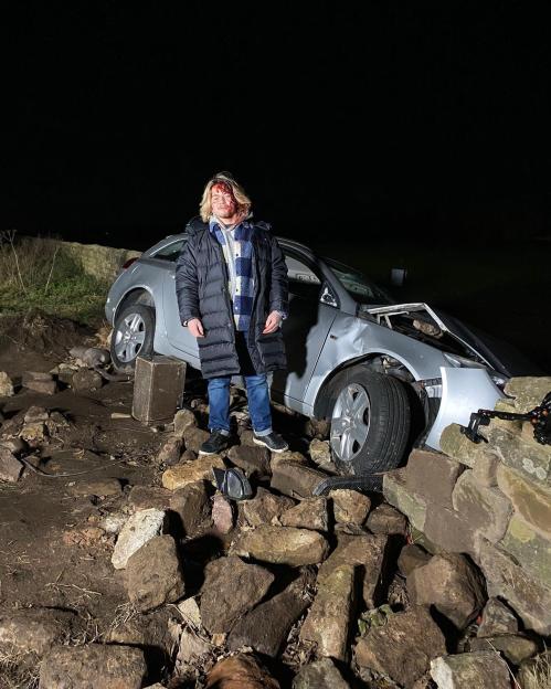Sebastian Dowling, injured, standing by a wrecked car.
