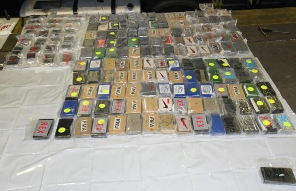 Seized blocks of illegal drugs, some marked "REX", "FMA", "007", "Nike swoosh", and "X2."