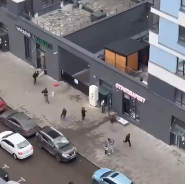 Aerial view of people running on a street with parked cars and shops.