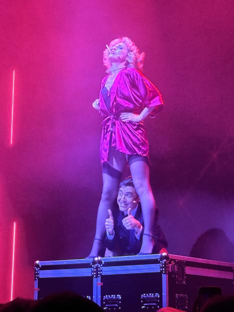 A man giving a thumbs up while a woman in a pink robe stands on a box above him.