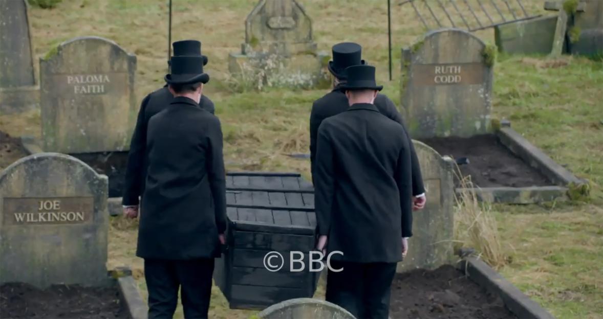 Three men in top hats carrying a coffin past tombstones for Paloma Faith, Ruth Codd, and Joe Wilkinson.